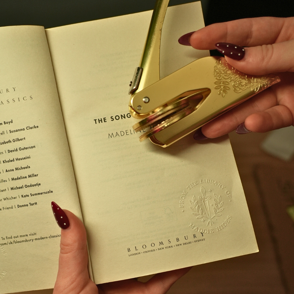 A custom brass book embosser beside a hardback book
