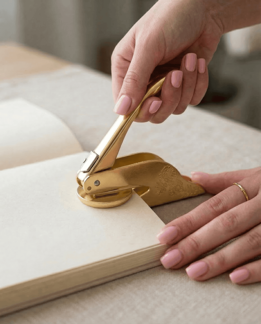 Hands pressing a gold book embosser onto the first page of a book