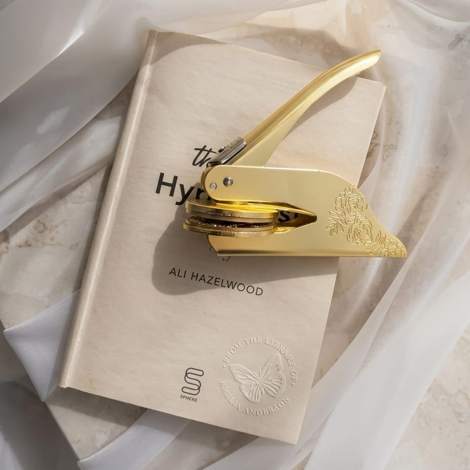A brass embosser resting beside a cream book with a butterfly seal pressed clean into the cover.
