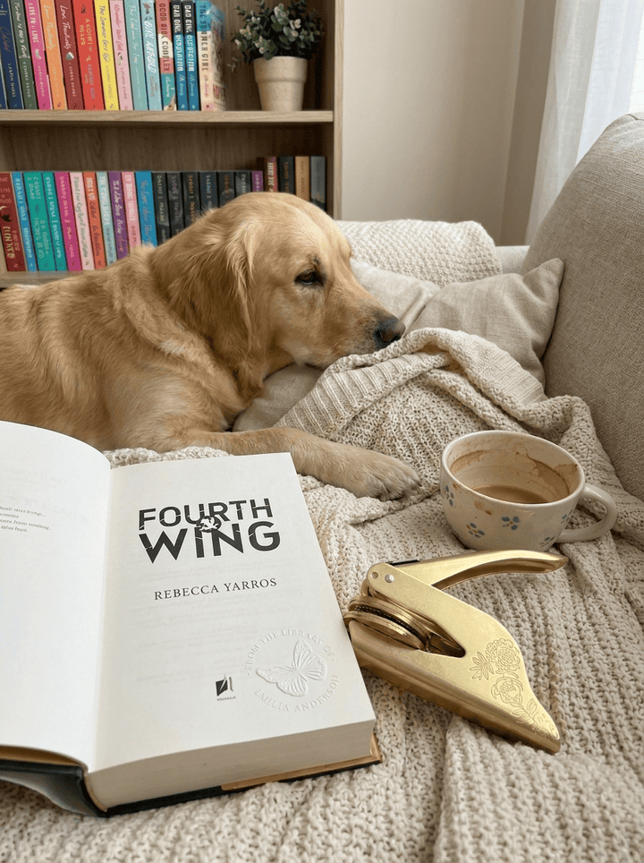A golden retriever asleep beside an open book and a gold embosser
